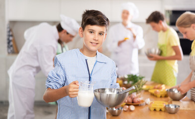 Cooking course - portrait of teenage boy in an apron who is learning to beat eggs to make pancakes...