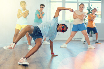 African boy in sun glasses performs choreographic exercises and teaches energetic mobile social dance Jazz-modern together with friends. Multi-racial group of children performs movements in studio