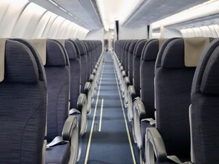 Inside passenger airplane - aisle and rows of seats, all in shades of grey colour. Empty