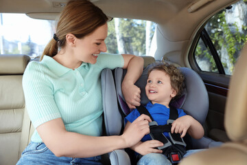 Mother fastening her son in child safety seat inside car