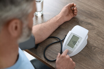 Man measuring blood pressure at table indoors, closeup
