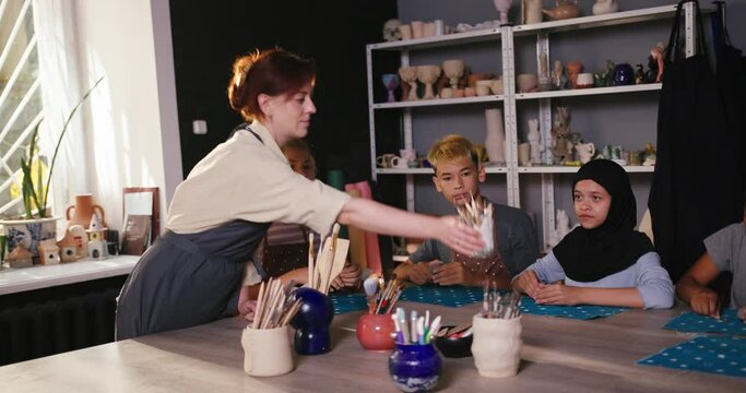 Teacher gives shaper sticks for pottery to smiling students
