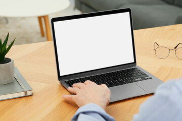 Man working with laptop at wooden table indoors, closeup