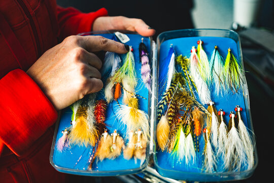 A hand points out bright streamers in a box of fly fishing lures