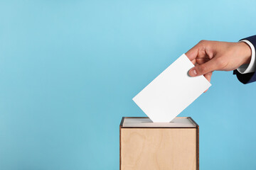 Man putting his vote into ballot box on light blue background, closeup. Space for text