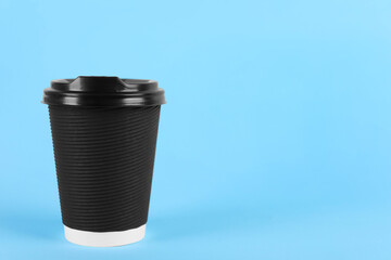 Black paper cup with plastic lid on light blue background, space for text. Coffee to go