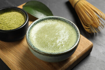 Cup of fresh matcha tea, bamboo whisk and green powder on black table, closeup