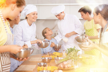 Obraz na płótnie Canvas Positive woman professional chef in white uniform conducting culinary class, imparting cooking skills to group of interested tween boys and girls