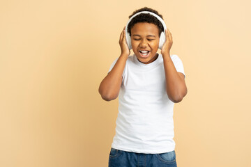 Portrait of cheerful smiling African American boy wearing headphones listening to music, singing...