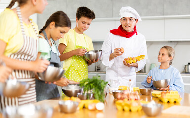 Young guy chef at master class teaches group of children how to cook food