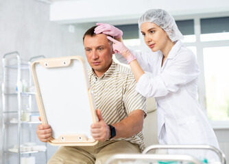 Girl doctor shows male patient areas of hair growth that require correction. Treatment of...