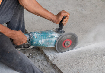 A worker cuts concrete floor with an electric circular saw.