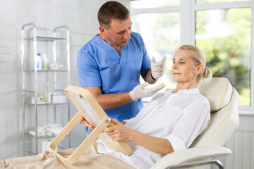 Obraz premium Beautician talking with patient before injection treatment, while client observing herself in mirror.