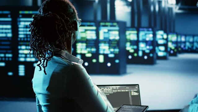 Adept african american technician programming scripts on tablet, updating data center infrastructure designed to accommodate modular servers, networking equipment and storage arrays