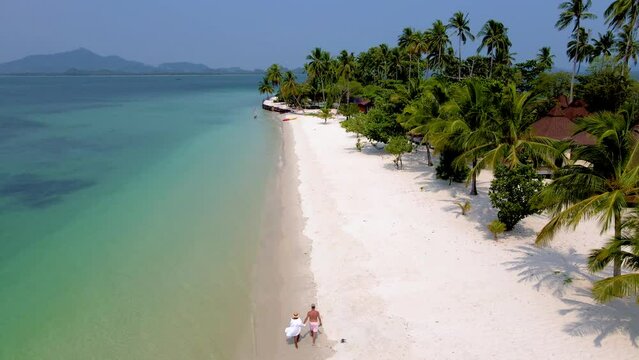 A couple of men and women on vacation at Koh Mook tropical Island in the Andaman Sea in Thailand, men and women walking on a beach with palm trees