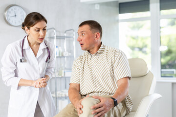 Female doctor carefully examining the sore leg of a male patient in the clinic