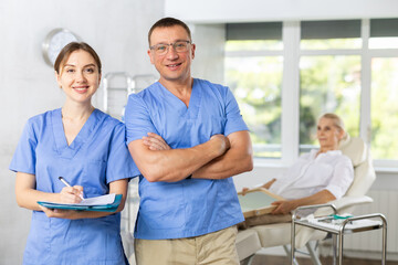 Obraz premium Middle-aged man and female doctor colleagues standing with documents after successful working day, receiving patients. Advertising poster of clinic