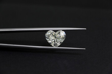 The big heart shape diamond in tweezers on black background