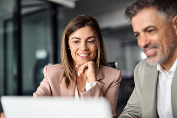 Smiling middle aged professional business woman executive working looking at laptop computer...