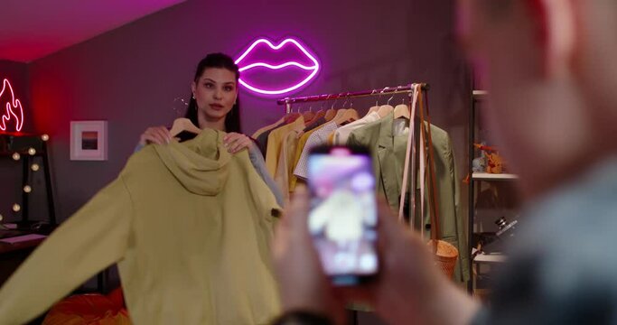 Video for social media female fashion blogger. Vertical video. Female is filming for shorts stories about fashion clothes in home studio. What to wear with what, fashion trends. Hands of assistant