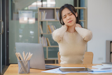 Overworked young Asian businesswoman office worker suffering from neck pain after having a long day at her office desk. office syndrome concept.