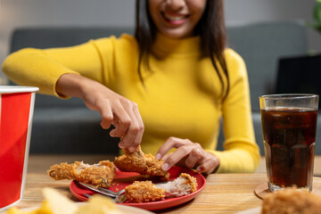 Happy Asian young woman eating delicious crispy fried chicken in the living room at home. family party Smile, laugh, enjoy food and drink, lifestyle concept, celebrate holidays.