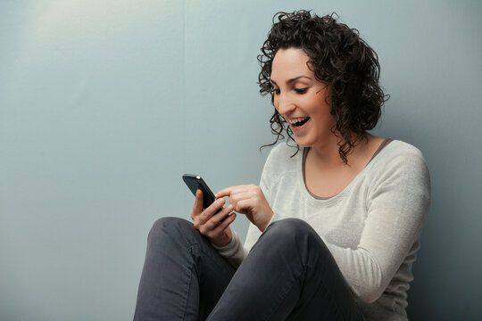 Seated by wall, she dives into smartphone