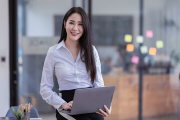 Portrait of a happy asian businesswoman working on laptop computer isolated over office background