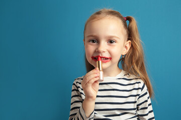 Happy little girl puts lipstick on her lips on blue background. Little trendy. little girl applying makeup