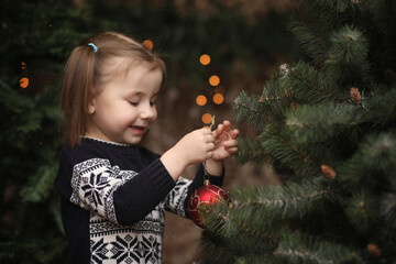 A little child by the New Year tree. Children decorate the Christmas tree. Baby in a sweater by a green tree in the studio.