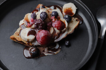 Rich crepe with lots of sweet chocolate and frozen red berries, on a black plate