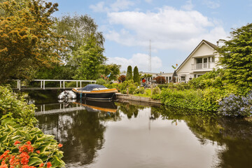 Obraz premium a canal with boats in the water and houses on both sides, surrounded by lush green trees and blue sky