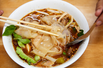 Wide rice noodles with braised chicken meat in a bowl