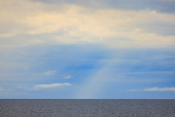 Rain falls from cloud layer over calm open ocean