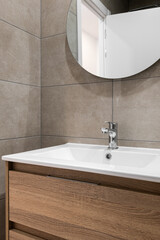 Modern bathroom with round mirror, wooden cabinet with drawers and white sink