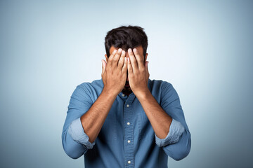 A man covering his face with his hands in front of a blue background, Generative AI