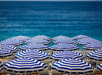 Pebble beach along Promenade des Anglais with beach umbrellas and chairs with the turquoise water of the Mediterranean Sea in Nice, Cote d'Azur France - obrazy, fototapety, plakaty