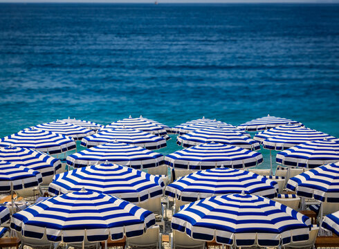 Pebble beach along Promenade des Anglais with beach umbrellas and chairs with the turquoise water of the Mediterranean Sea in Nice, Cote d'Azur France