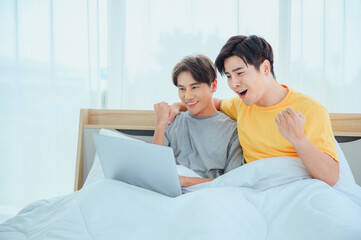 Asian couple having fun using laptop in bed in the morning