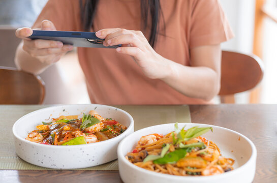 Asia woman eat lunch with feeling happy and enjoy to eat shrimp spaghetti stir fry in restaurant in relax fun with cell phone take a photo of her food for upload to social media. Enjoy food concept.