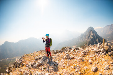 Fototapeta premium hiking in the mountains. a girl with a backpack takes pictures of the mountains and the sky on the phone from the top of the mountain. climbing and hiking.