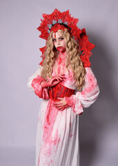 Close up portrait of  scary vampire zombie queen, wearing elegant halloween fantasy costume with crown and bloody red paint splatter. Isolated on studio background with gestural hands reaching out tow