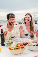 Vertical portrait of a happy young adult couple smiling and dining with their friends on a friendly lunch party celebration. Family people feeding celebrating a barbeque event with their buddies. High