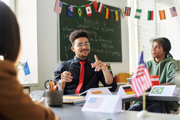 Smiling teacher talking about holiday to students during lesson while they sitting at desk in class
