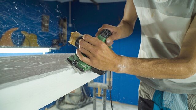 Male surfboard shaper making surfboard in his workshop. Hand shaping from blank.