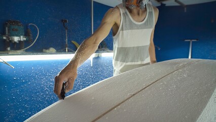 Male surfboard shaper making surfboard in his workshop. Hand shaping from blank.