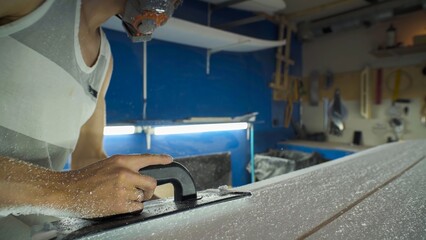 Male surfboard shaper making surfboard in his workshop. Hand shaping from blank.