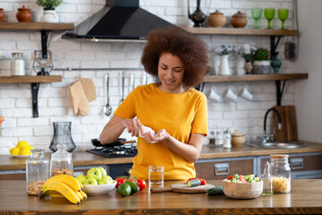 Happy african american woman standing at the cuisine table at home kitchen drinking dietary supplements. Healthy concept
