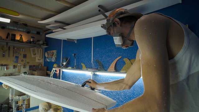 Male surfboard shaper making surfboard in his workshop. Hand shaping from blank.