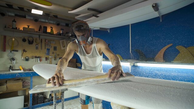Male surfboard shaper making surfboard in his workshop. Hand shaping from blank.